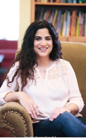 Author Hena Khan smiles as she sits in an armchair