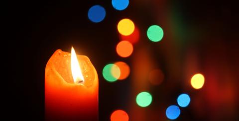 Candle with flame and colored lights in the background