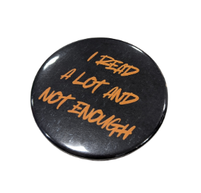 Photo of a 2.25 inch button with a black background and orange that reads "I READ A LOT AND NOT ENOUGH"