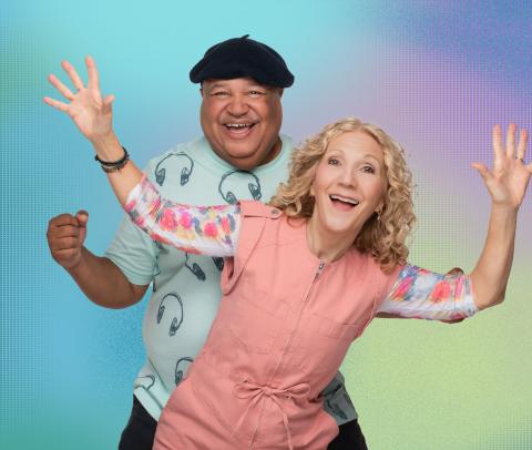 Musicians DB, a man wearing a hat, and Wendy, a woman in a pink blouse mug for the camera.