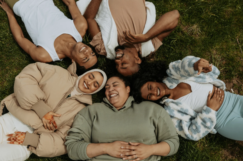 Five people laying on the ground with their heads touching in a circle smiling