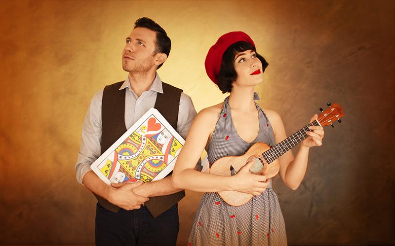 Two magicians posing with an oversized playing card and a ukulele