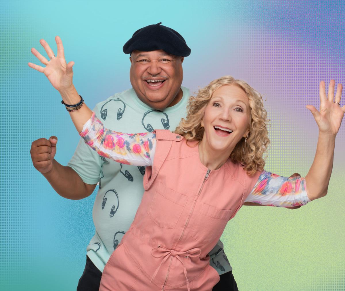 Musicians DB, a man wearing a hat, and Wendy, a woman in a pink blouse mug for the camera.